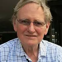 Patrick Casement has short grey hair. He is wearing thin, rectangular glasses and a blue checked shirt