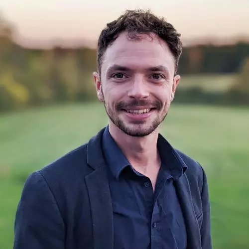 Hal Cooper, with short brown hair, is wearing a dark blue shirt and jacket, smiling at the camera