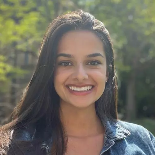 A headshot of Deanna Giraldi, with long dark shoulder-length hair, shows her smiling while wearing a denim jacket and looking directly at the camera.