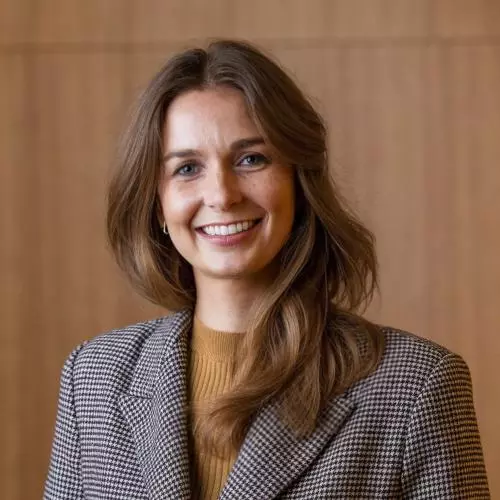 Cyrette Saunier wears a grey blazer and is smiling in front of a wood-panelled wall.