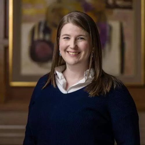 Julia has shoulder length ginger brown hair, with a dark top smiling at the camera.