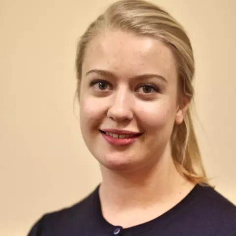 katariina has long blonde hair tied back in a ponytail. She's wearing a buttoned-up navy blue cardigan