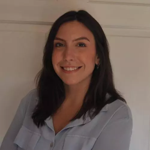 Luciana Leite has long dark hair and is wearing a light blue blouse. She is smiling at the camera.