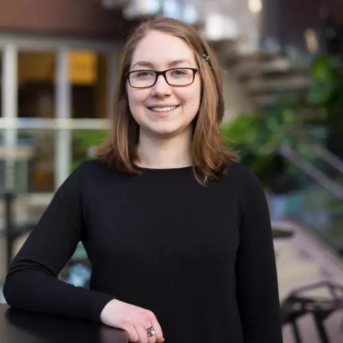 Mackenzie Martin has shoulder length brown hair with a hair clip at the side. She is wearing glasses and a black long-sleeved top