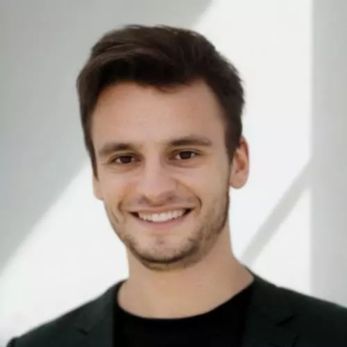 Michael Ganslmeier has short dark hair, dark eyes and dark facial hair. He is wearing a black t-shirt and smiling. 