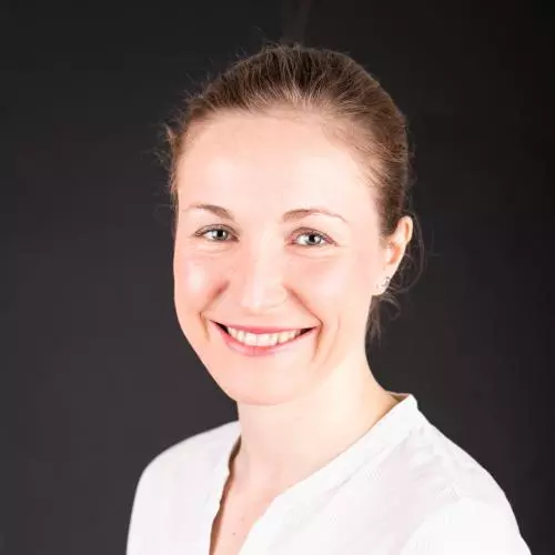 Rachel has brown hair that's tied back in a pony tail,  and she's smiling at the camera.  She's wearing a white blouse. 