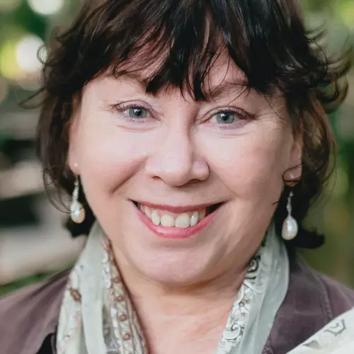 Woman with short brown hair, smiling broadly with a light green patterned scarf around her neck.