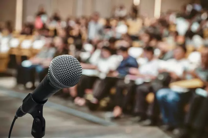 A close up of a microphone, in front of a large seated audience. Credit: Tzido - Getty Images-829570660