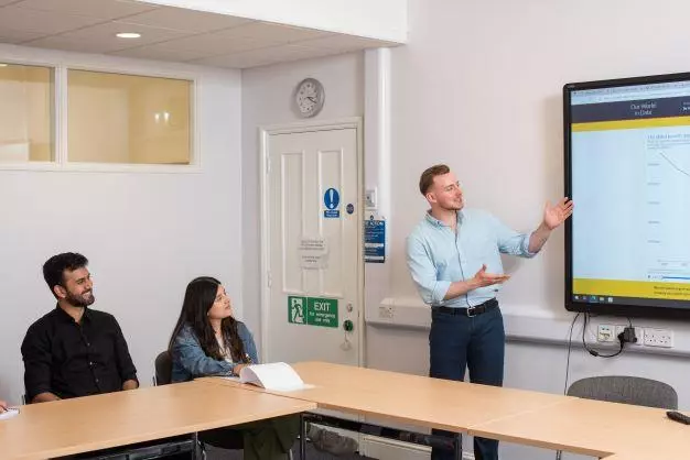 DSPI students in a lecture room with a tutor standing next to a large screen on the wall