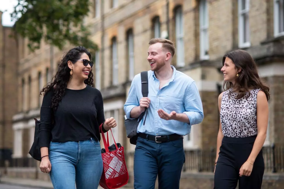 Two women and a man walking down a street, looking at each other, chatting and smiling. 