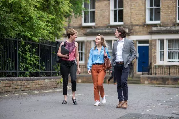 Three students walking down a street, looking at each other and chatting