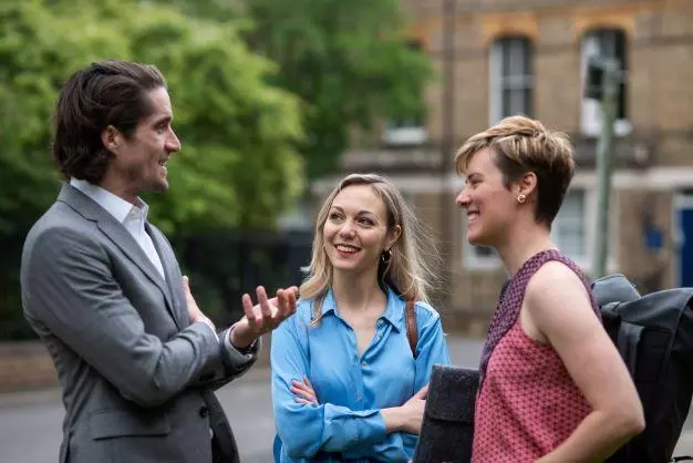 Students chatting with an academic outside in front of buildings and a tree